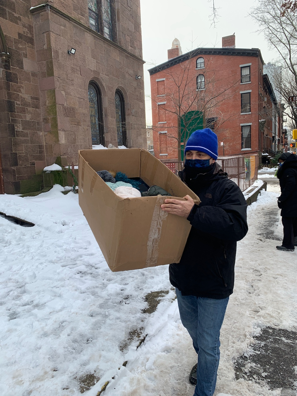 Man on the sidewalk carrying box of donated coats during 2020 drive.