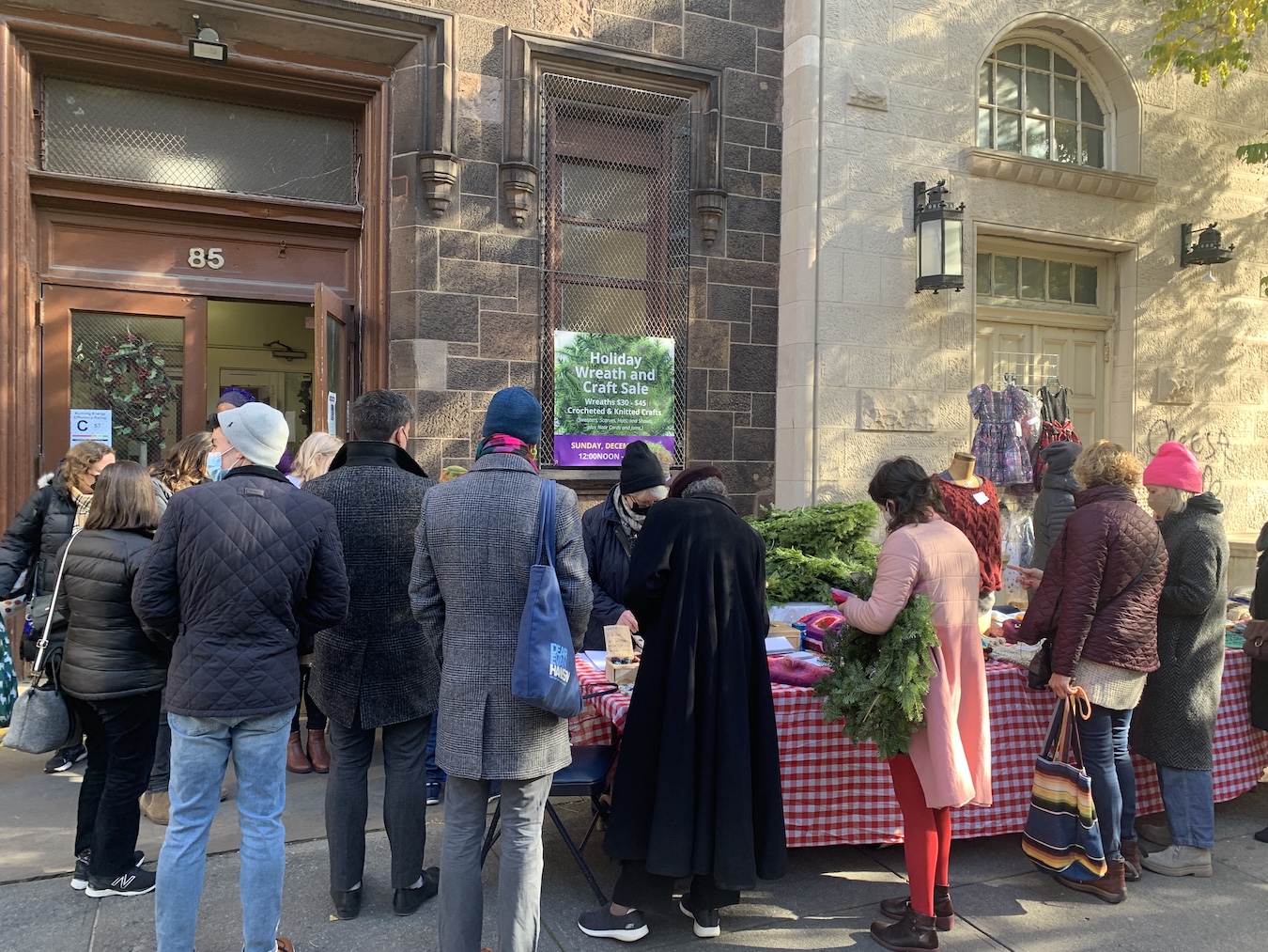 People in winter coats, outside the church shopping the table of craft items.