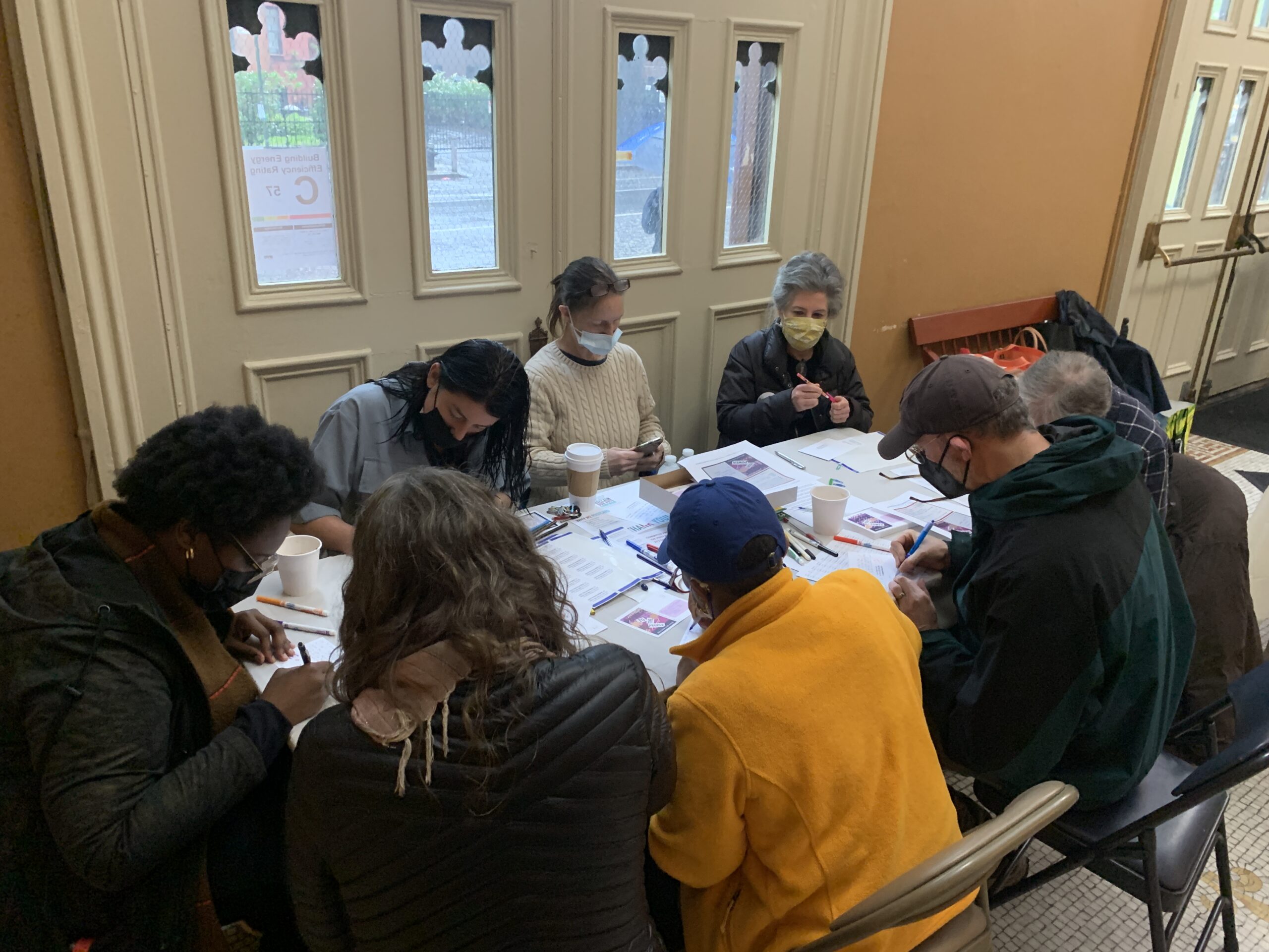 People gathered around a folding table inside a church entrance. On the table are postcards and papers they are filling out.