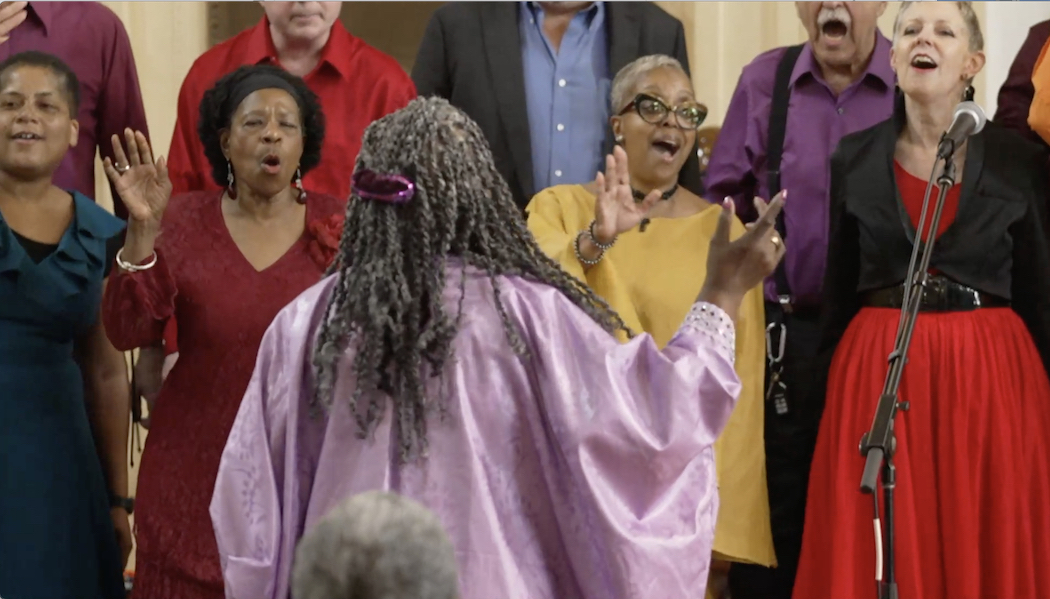 Photo of members of the choir singing, choir director in foreground with back to camera.