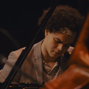 Photo of musician Tyler Bullock at the piano, in the foreground part of a stand-up bass
