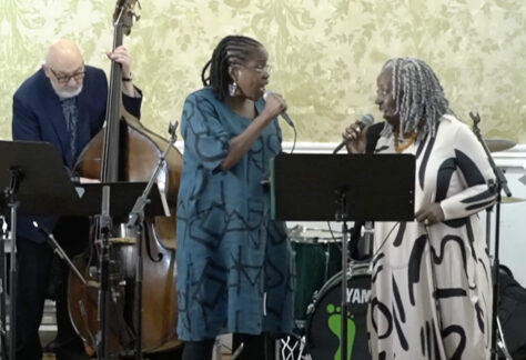 Three jazz musicians performing indoors, one on a stand-up bass, and two vocalists