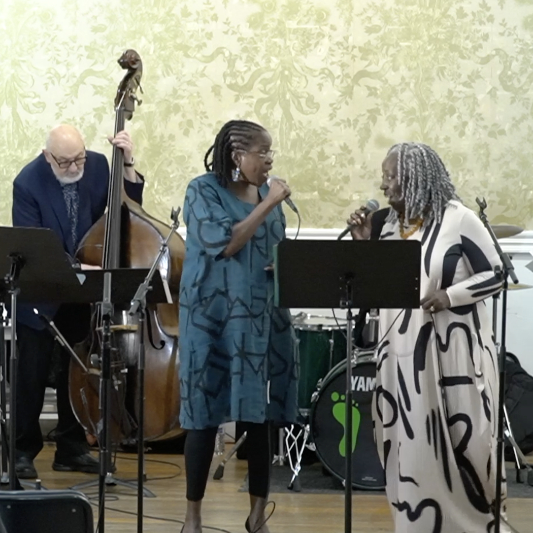 Three jazz musicians performing indoors, one on a stand-up bass, and two vocalists