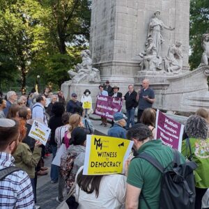 Crowd gathered in front of statue, many holding protest signs
