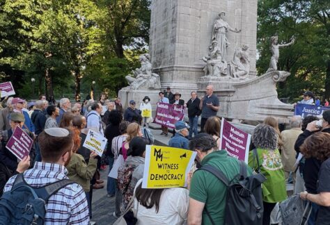 Crowd gathered in front of statue, many holding protest signs