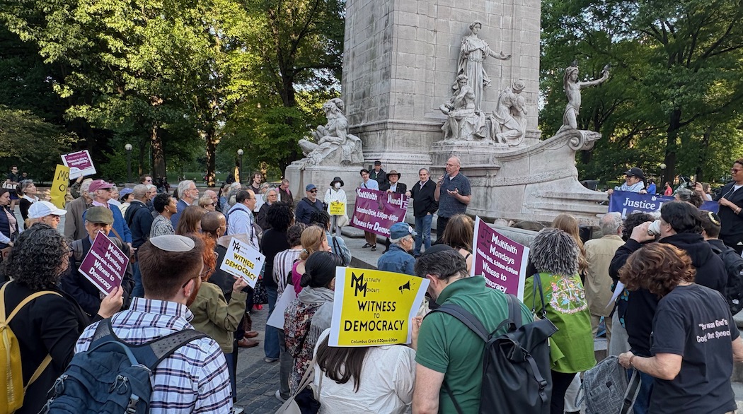 Crowd gathered in front of statue, many holding protest signs