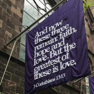 Flag on front of church building with scripture reading "And now these three remain: faith, hope and love. But the greatest of this is love. 1Corinthians 13:13