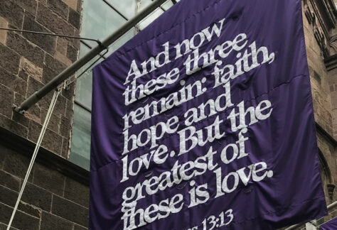 Flag on front of church building with scripture reading "And now these three remain: faith, hope and love. But the greatest of this is love. 1Corinthians 13:13