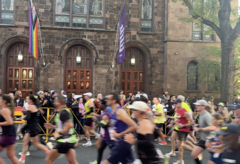 Athletes running in the street past a church, crowd cheering. A scene from the NYC Marathon