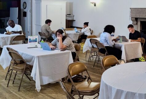 People in a room, gathered on tables, working on computers